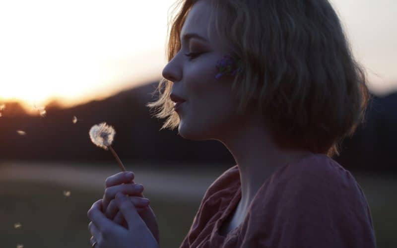 nainen puhaltaa voikukan hahtuvia